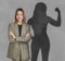 Businesswoman and shadow of strong muscular lady behind her on grey wall. Concept of inner strength