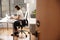 Businesswoman Sitting At Desk Working On Laptop In Modern Office Viewed Through Door Way