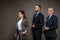 Businesswoman standing with hand in pocket near businessmen touching suits on grey