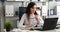 Businesswoman taking off glasses and looking into camera, working on laptop in modern office.