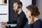 Businesswoman talking by headset while sitting with red-bearded colleague in modern office. Telemarketing and customer