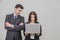 Businesswoman using laptop. Man on her side standing with his hands folded. Both seem to be annoyed and disappointed.