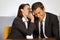 Businesswoman whispering in businessman\'s ear at office