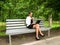 Businesswoman working on laptop sitting on a bench in the park. Cute young adult girl in a little black dress, white jacket and