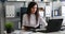 Businesswoman working on laptop and writing on paper in modern office.