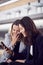 Businesswomen Commuting To Work Wait For Train On Station Platform Looking At Mobile Phone Together