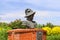 A bust statue of a Spanish explorer on the Savannah riverfront surrounded by red brick and lush green plants and yellow flowers