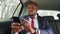 Busy african executive in car typing text message on phone