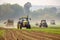 Busy agricultural scene with tractors and farm workers harvesting crops in a vast farmland