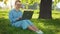 Busy attractive woman working at the laptop as sitting on grass in city park