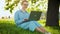 Busy attractive woman working at the laptop as sitting on grass in city park