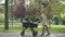 Busy Caucasian businesswoman talking on the phone and rocking baby stroller. Wide shot side view of elegant slim woman