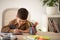 Busy cheerful cute small european boy sitting at table, draws picture in room, children garden or school interior