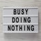 `Busy doing nothing` words on modern board on a white wooden surface, top view. From above, flat lay, overhead