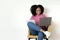 Busy happy millennial african american curly lady in casual sits on armchair, typing at computer