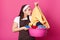 Busy housewife holds basin of dirty clothes, does washing during weekend, smells shirt, dressed in casual apron and headband,