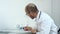 Busy male physician working with medical forms and papers in hospital office room