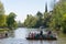 Busy manual ferry crosses busy river with trees and church in background