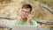 Busy mature man working on a laptop computer with business papers picking up a phone to work a call sitting on the beach