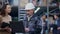 Busy senior man in hard hat using laptop as cheerful young beautiful woman approaching talking and laughing. Portrait of