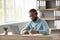 Busy serious millennial african american bearded guy in glasses and headset working on laptop in home