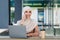 Busy smiling attractive young arab lady in hijab calls on phone, sits with laptop and coffee in cafe