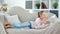 Busy thoughtful young female child reading book lying on couch at cozy living room full shot