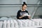 Busy woman standing behind rows of blank cups in workshop, filling in paperwork