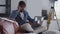 Busy young African American man receiving phone call sitting on couch in home office with laptop. Portrait of confident