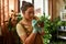 Busy young female gardener wearing protective gloves using cotton bud to clean green leaves of houseplant