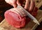 Butcher slicing Fresh Raw top side beef meat on rustic wooden chopping board