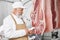 Butcher in white uniform testing pork carcasses with device.