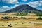 A butte mesa sitting majestically on a wide open wester landscape - hills, hay rolls, farm