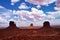 Butte rock formations with dirt road, shadows and fluffy clouds in Monument Valley, Arizona
