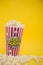 Butter popcorn in a red popcorn cup, snack in the house or cinema on a yellow background