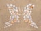 Butterfly or two profile side silhouette created of sea shells on sand background. Top view optical illusion appropriate to