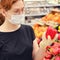 A buyer in a medical mask chooses vegetables in a supermarket. Selling vegetables and fruits in the store