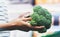 The buyer weighs the green fresh broccoli close up, woman shopping healthy food in supermarket blur background, female hands buy