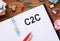 C2C abbreviation - consumer to consumer - printed on a clipboard lying on wooden desk with colourful staples, paper stick notes,