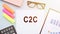 C2C Client To Client acronym on white notepad next to glasses, calculator and color markers