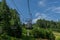 cable car construction with wires and empty seats among green trees, grass field in forest on hill, summer