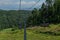 Cable car empty seats among trees, grass field in green forest on hill, sunny summer blue sky with white clounds, baikal lake