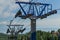 cable car pillars constructions among trees in green forest on mountain, blue sky with clounds, lake on horizon