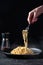 Cacio e Pepe - Hot Italian Pasta with Cheese and Pepper on Black Plate, Woman Holding Fork Spaghetti on Dark Background