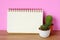 Cactus, succulent plants and blank notebook paper on wooden table and pink background, desert houseplant trendy design background