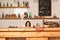 Cafe owner near table with salt and pepper mills, jar, bowl with fruits and card with closed inscription