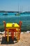 Cafe tableon beach in Adamantas town on Milos island with Aegean sea with boats in background