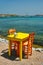 Cafe tableon beach in Adamantas town on Milos island with Aegean sea with boats in background