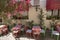 Cafe tables and chairs and pink flowers in the street. People walking on the street