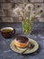 Cake Bush on a small plate with a mug of tea and a bunch of dandelion balls in a glass beaker